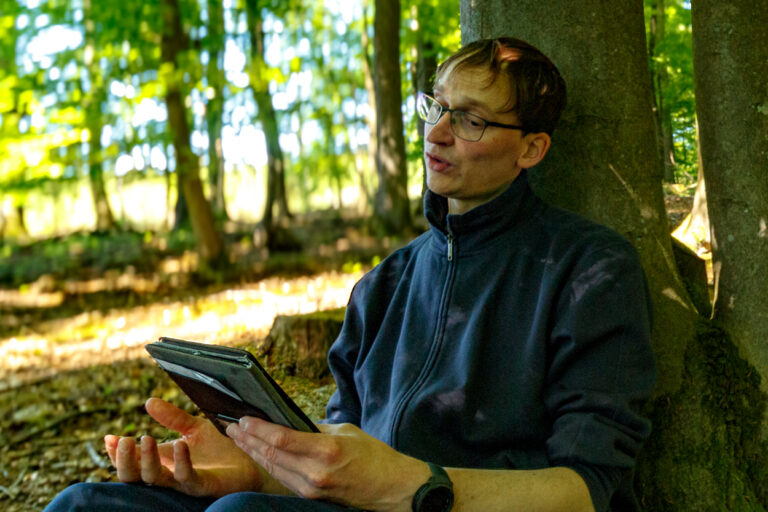 Profilbild, Christian Scholz, wie er als Trainer während eines Seminars im Wald, den Teilnehmenden etwas erklärt.